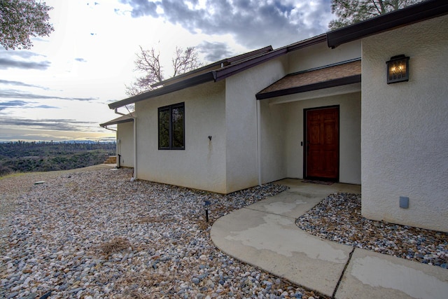 doorway to property featuring roof with shingles and stucco siding