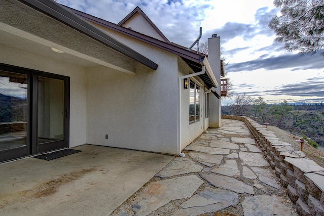 view of side of home featuring a chimney, a patio area, and stucco siding