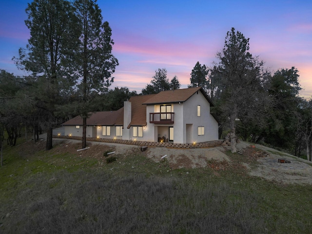 view of front of property with a front yard, a chimney, a balcony, and stucco siding