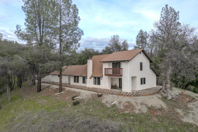 back of house featuring a balcony, a chimney, and stucco siding