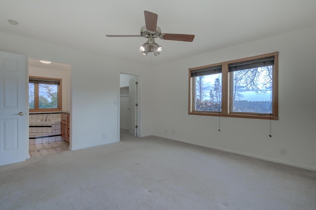 unfurnished bedroom featuring light carpet, a ceiling fan, baseboards, a spacious closet, and ensuite bath