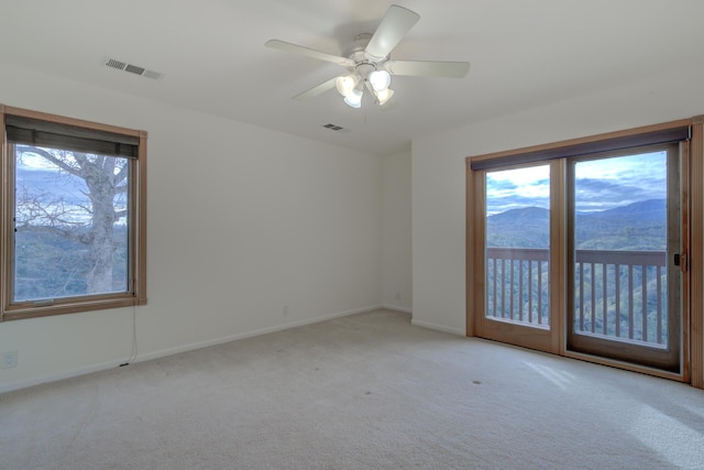 unfurnished room with light colored carpet, visible vents, a mountain view, and baseboards