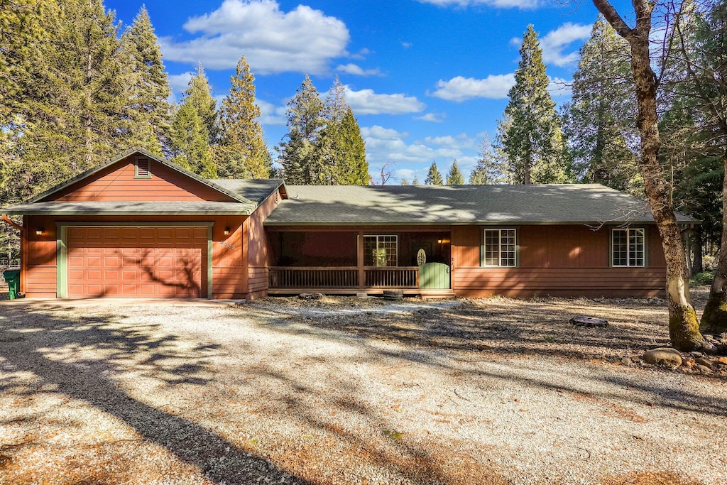 ranch-style home featuring covered porch, gravel driveway, and a garage