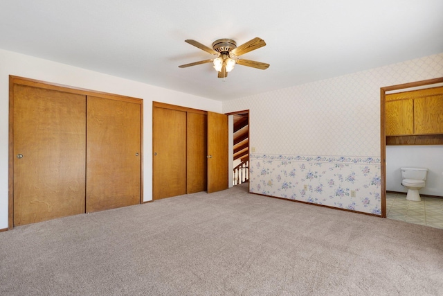 unfurnished bedroom featuring light carpet, connected bathroom, two closets, and ceiling fan