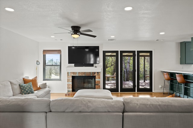 living room featuring ceiling fan, a textured ceiling, a brick fireplace, and light wood-type flooring