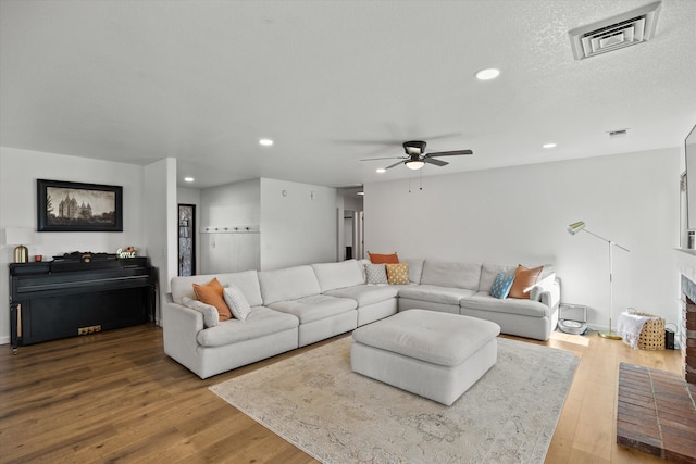 living room featuring ceiling fan, hardwood / wood-style floors, a textured ceiling, and a fireplace