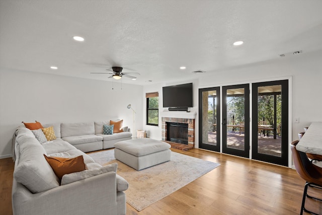 living room with light hardwood / wood-style flooring, ceiling fan, a brick fireplace, a textured ceiling, and french doors