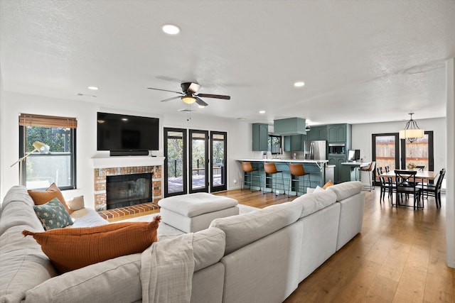 living room featuring a brick fireplace, light hardwood / wood-style flooring, a textured ceiling, and ceiling fan