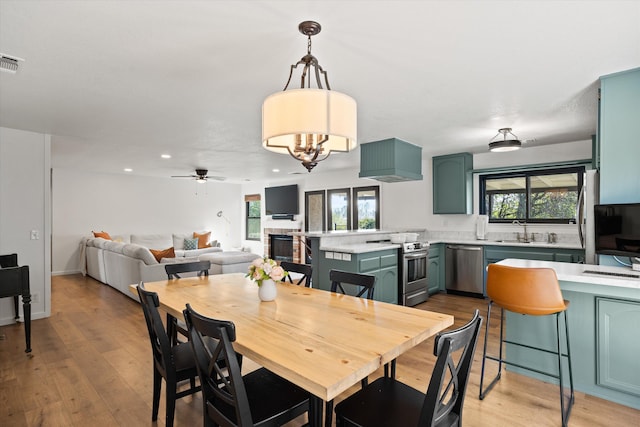 dining area featuring sink, ceiling fan with notable chandelier, and light hardwood / wood-style floors