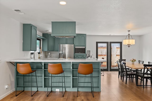 kitchen with pendant lighting, stainless steel fridge, kitchen peninsula, and wood-type flooring