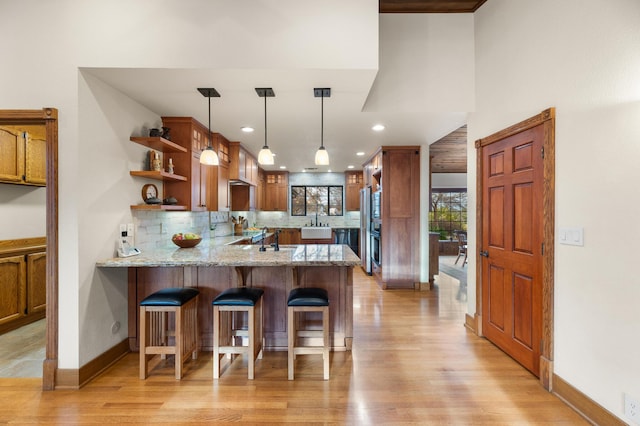 kitchen with tasteful backsplash, decorative light fixtures, a peninsula, light wood-style floors, and a kitchen bar