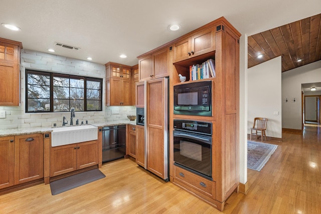 kitchen with glass insert cabinets, brown cabinetry, a sink, light stone countertops, and black appliances