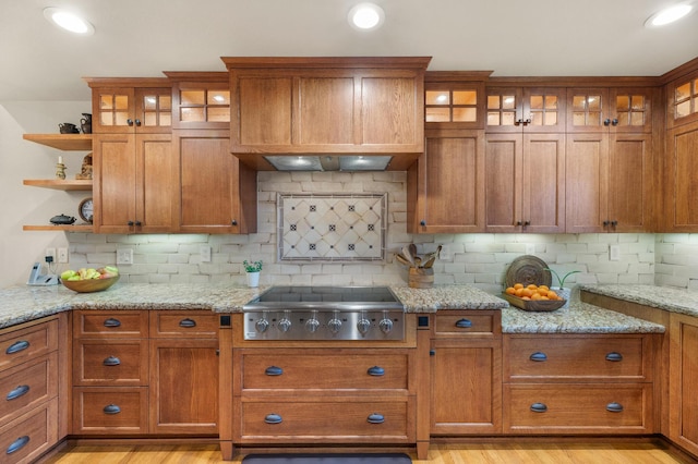 kitchen with light wood-type flooring, stainless steel gas cooktop, brown cabinets, and light stone counters