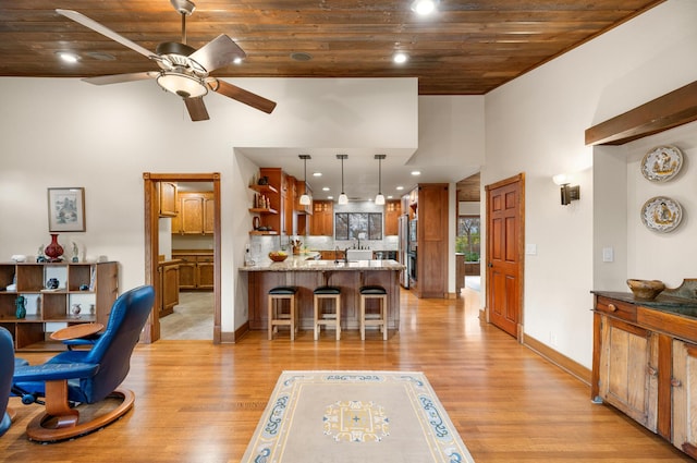 living room with a high ceiling, a ceiling fan, light wood-type flooring, wooden ceiling, and baseboards