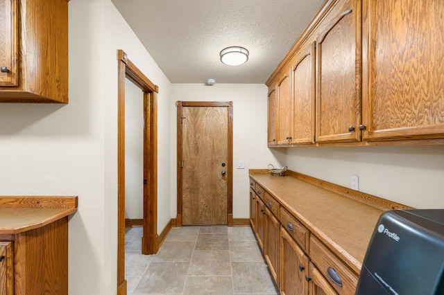 kitchen featuring brown cabinetry, light countertops, a textured ceiling, and baseboards