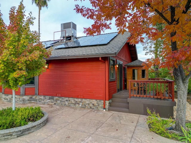 view of side of home with a shingled roof, cooling unit, and roof mounted solar panels