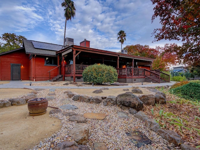 view of front of property with solar panels, a porch, a chimney, and central air condition unit