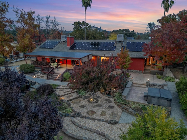 back of house at dusk with a chimney, roof mounted solar panels, a deck, driveway, and stairs