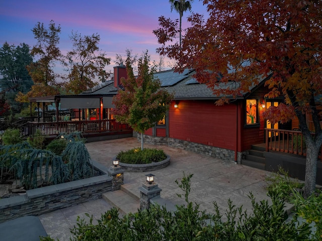 back of house at dusk with a patio and roof mounted solar panels