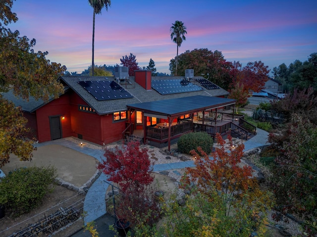 view of front facade featuring driveway, central air condition unit, roof with shingles, and roof mounted solar panels