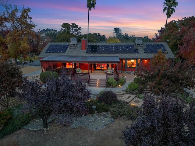 back of property at dusk featuring roof mounted solar panels and a deck