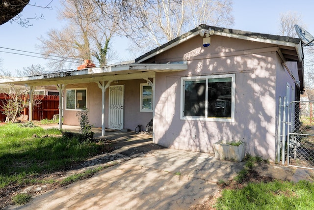 view of front facade with covered porch, fence, and stucco siding