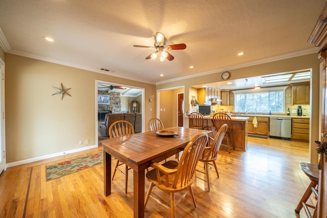 dining space featuring light wood-style flooring, visible vents, ornamental molding, and a stone fireplace