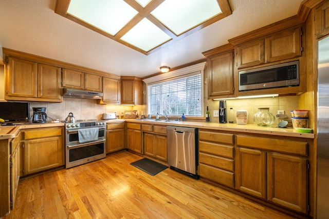 kitchen featuring light countertops, appliances with stainless steel finishes, brown cabinetry, and under cabinet range hood