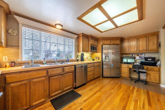 kitchen featuring brown cabinets, stainless steel appliances, light countertops, built in study area, and a sink