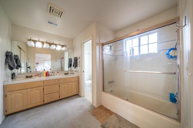 full bath with toilet, a sink, visible vents, combined bath / shower with glass door, and double vanity