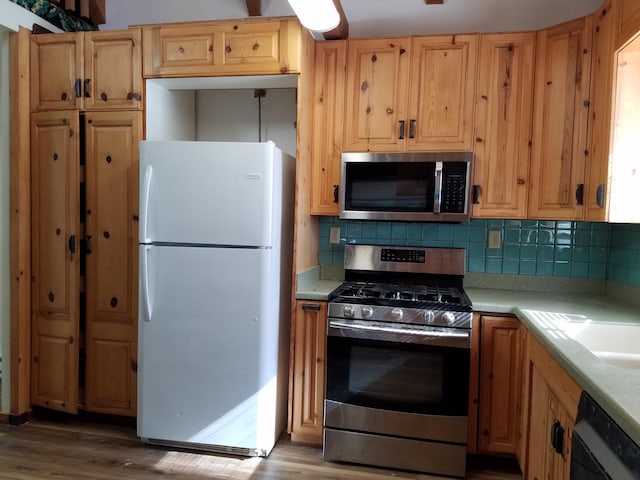 kitchen with light countertops, wood finished floors, stainless steel appliances, and backsplash