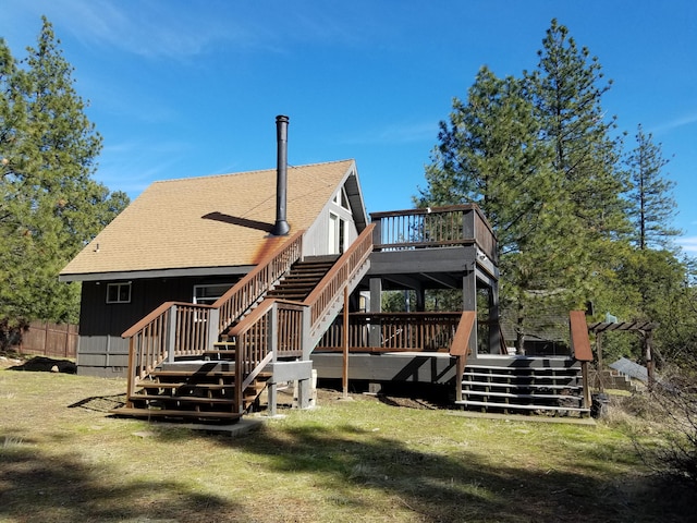 rear view of property featuring a yard, a wooden deck, and roof with shingles