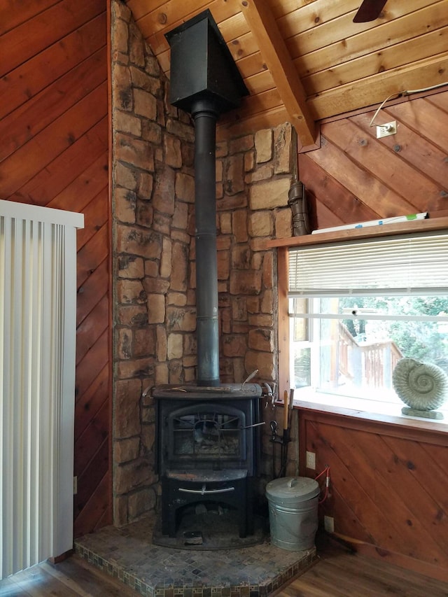 details with beam ceiling, wood finished floors, wood walls, and a wood stove