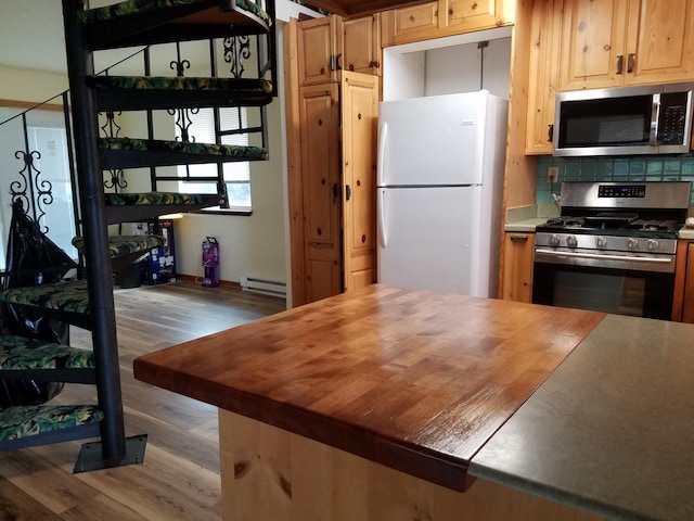 kitchen with tasteful backsplash, butcher block countertops, baseboard heating, appliances with stainless steel finishes, and wood finished floors