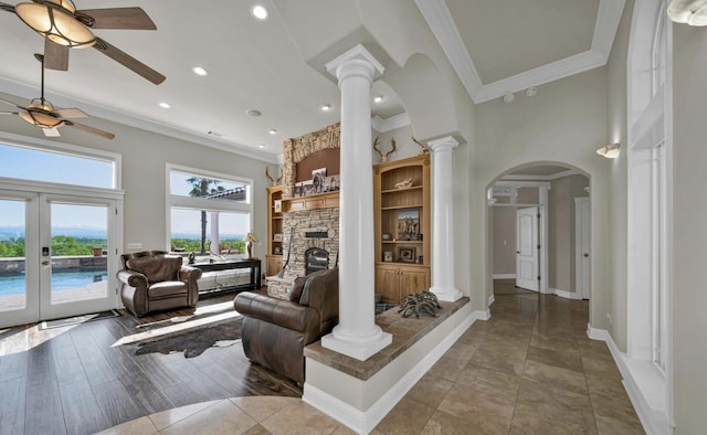 tiled living room featuring a stone fireplace, crown molding, ornate columns, and french doors