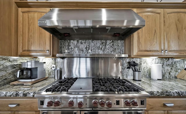 kitchen with exhaust hood, dark stone counters, high end stainless steel range, and backsplash