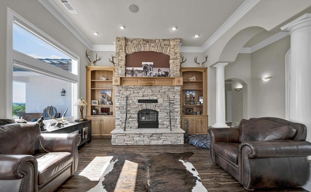 living room with crown molding, dark hardwood / wood-style flooring, decorative columns, and a stone fireplace