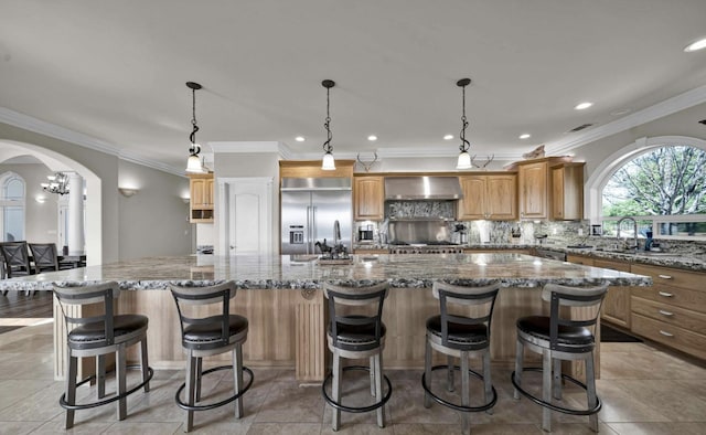 kitchen featuring stainless steel built in refrigerator, a breakfast bar area, a large island, wall chimney exhaust hood, and decorative light fixtures