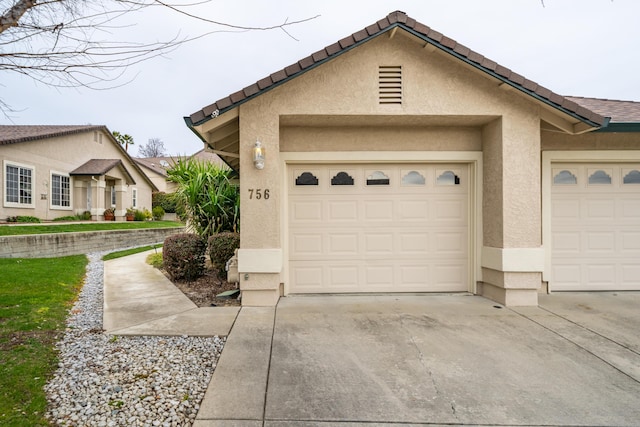 exterior space featuring concrete driveway, a tiled roof, an attached garage, and stucco siding