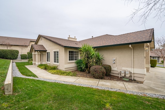 exterior space with a shingled roof, a lawn, a chimney, and stucco siding