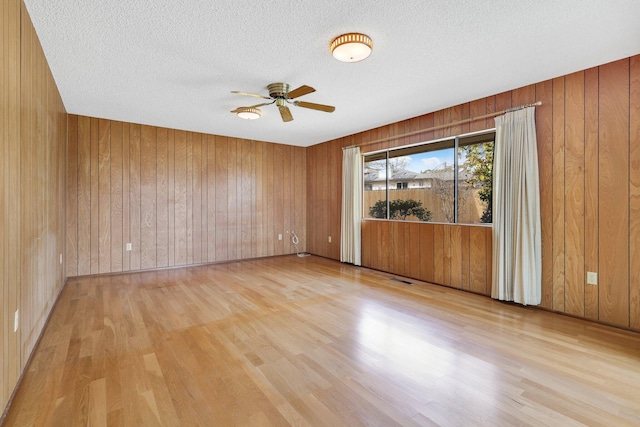 empty room with ceiling fan, light hardwood / wood-style floors, a textured ceiling, and wooden walls