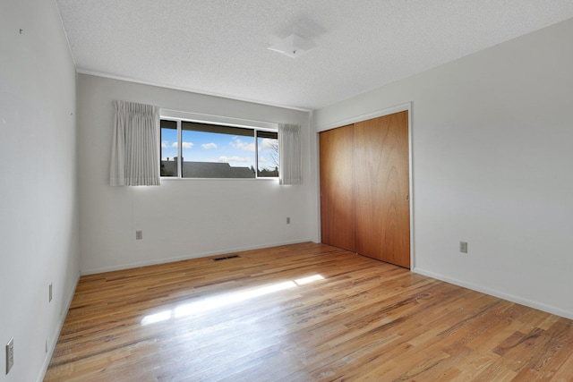 unfurnished bedroom with light hardwood / wood-style floors, a textured ceiling, and a closet