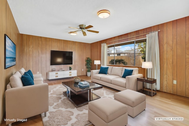 living room featuring ceiling fan, light hardwood / wood-style flooring, and wooden walls