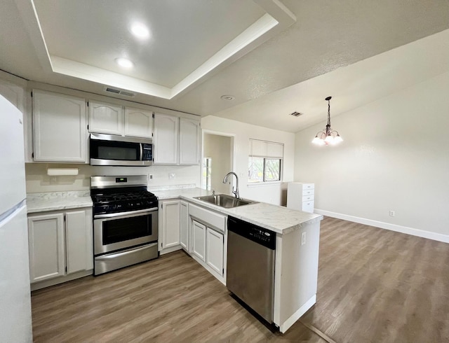 kitchen with sink, decorative light fixtures, stainless steel appliances, kitchen peninsula, and white cabinets