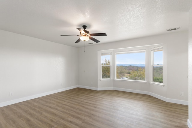 empty room featuring a mountain view, ceiling fan, wood-type flooring, and a textured ceiling