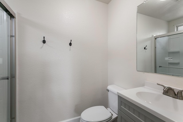 bathroom featuring vanity, a shower with door, and toilet