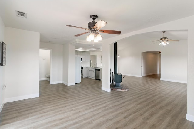 unfurnished living room featuring a wood stove, light hardwood / wood-style floors, vaulted ceiling, and ceiling fan