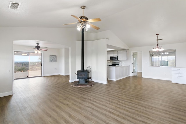 unfurnished living room featuring ceiling fan, a wood stove, vaulted ceiling, and dark hardwood / wood-style flooring