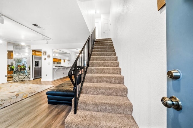 staircase featuring baseboards, track lighting, visible vents, and wood finished floors