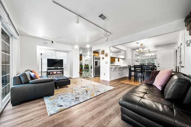 living area featuring light wood-type flooring, visible vents, a notable chandelier, and baseboards